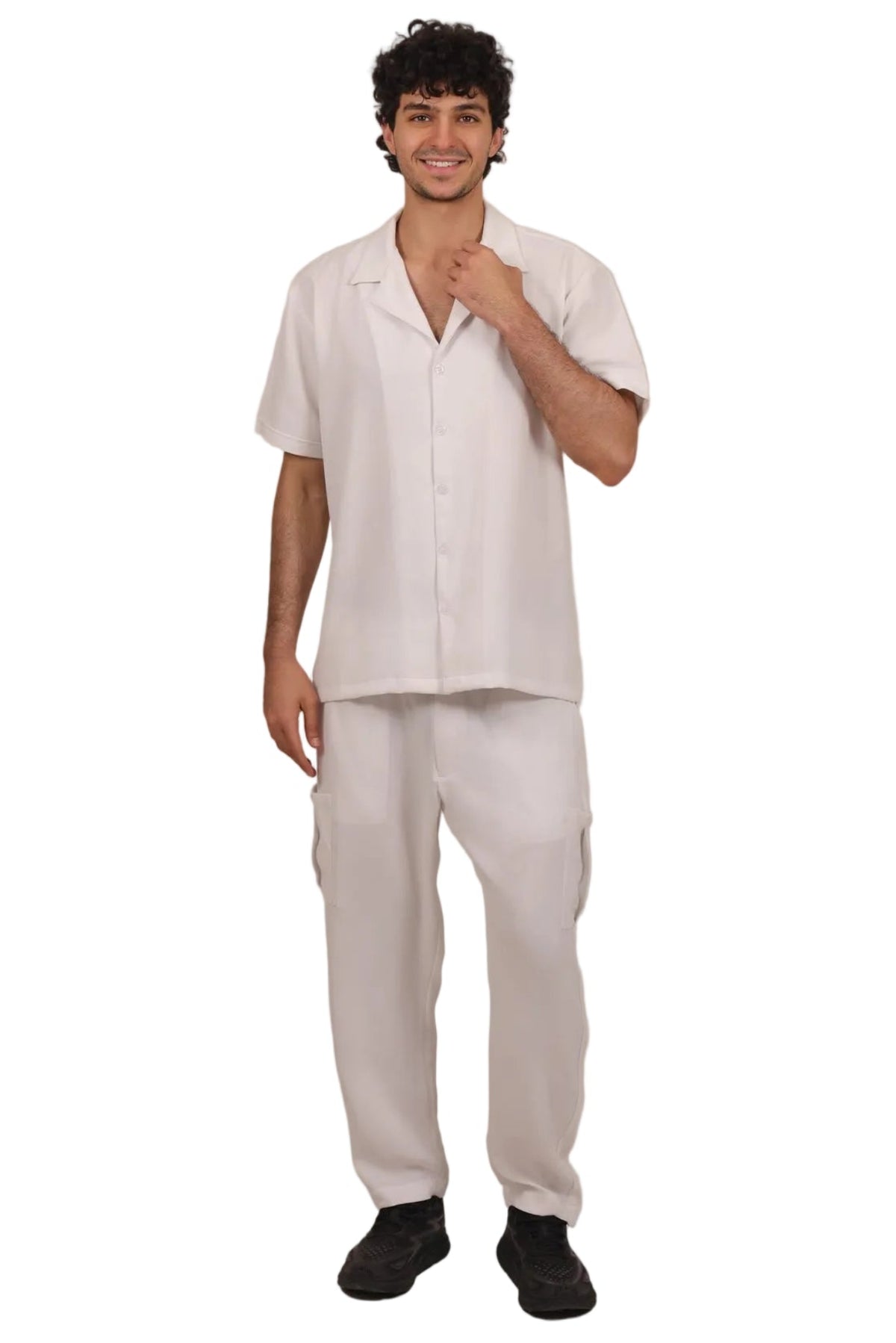 A man modeling a light beige short-sleeve camp shirt and matching cargo pants against a solid white background.