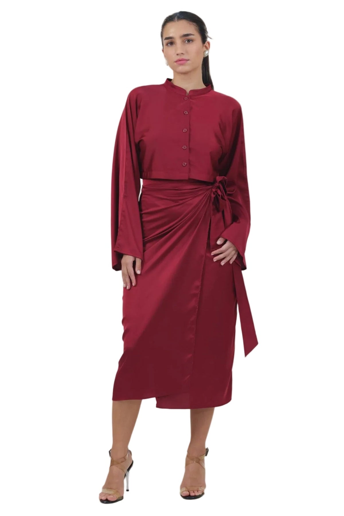 A woman modeling a long-sleeved, midi-length wrap dress in deep burgundy. The dress features a button-up front, a high collar, and a matching fabric tie belt at the waist.