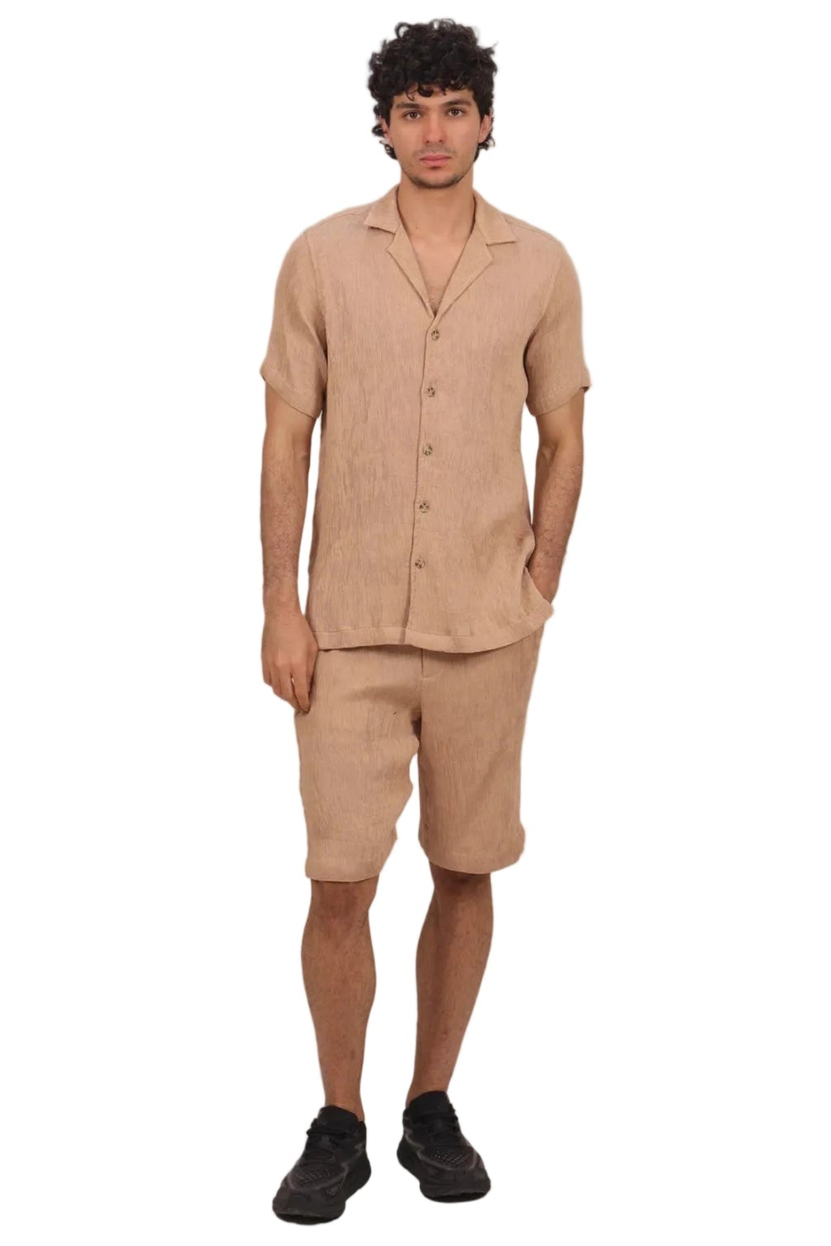 A man modeling a matching beige linen short-sleeve button-up shirt and shorts set, paired with black sneakers, against a solid white background.