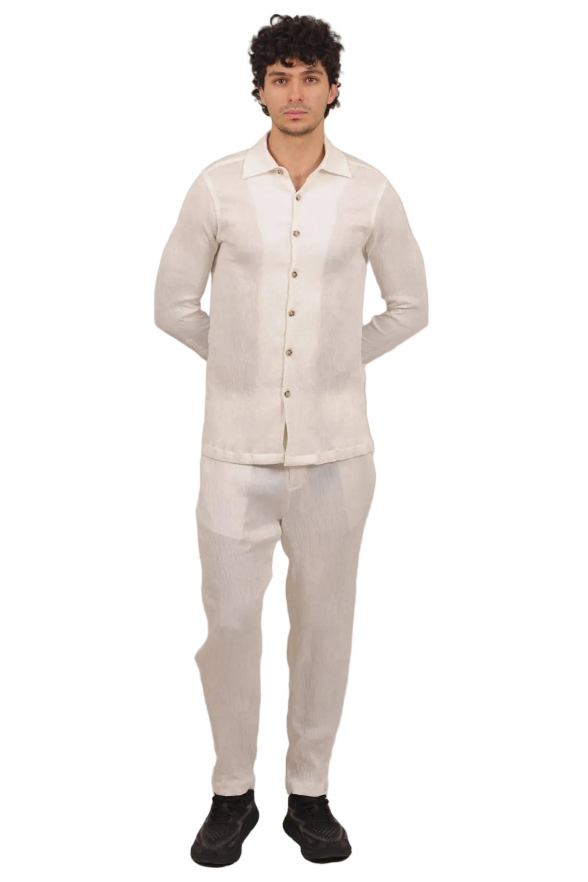 A man modeling a light beige two-piece linen set consisting of a long-sleeve button-up shirt and matching trousers, standing against a solid white background.