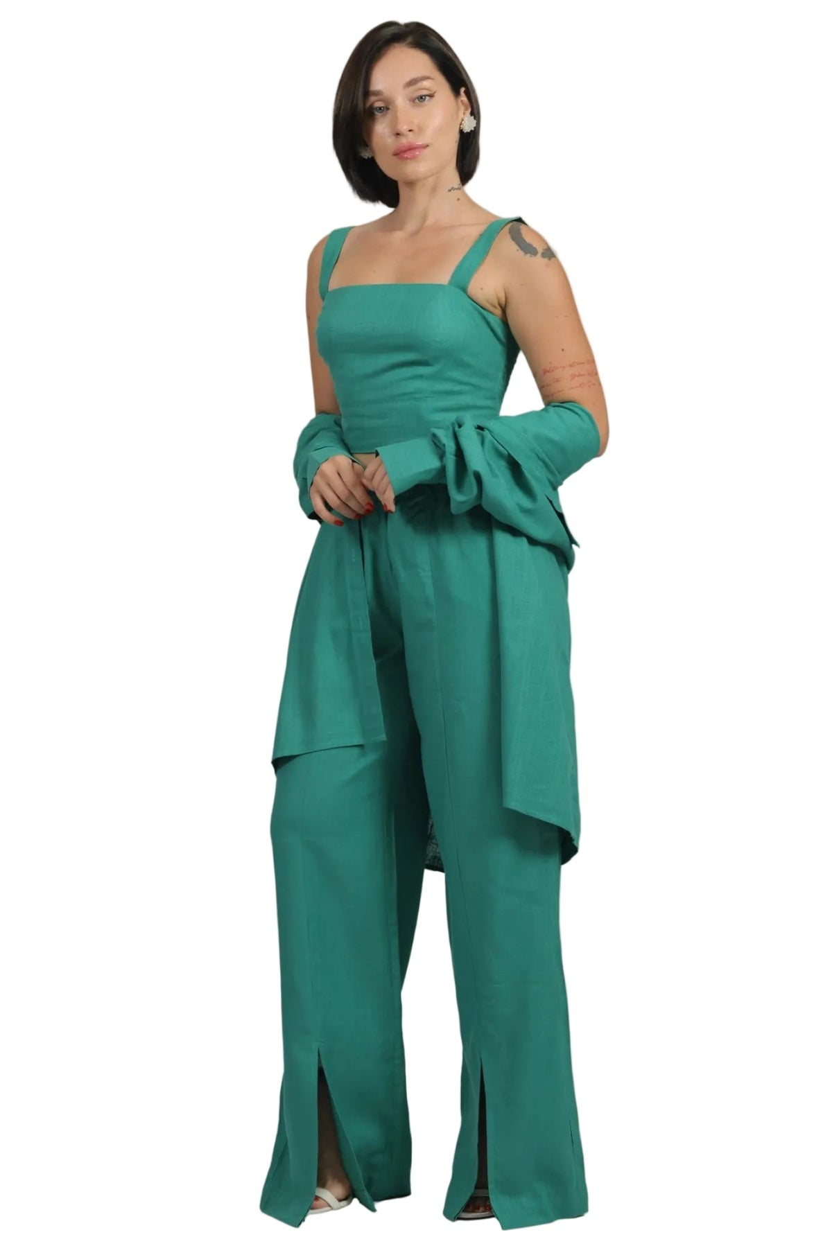 A woman modeling a teal green one-piece jumpsuit with wide-leg pants, a structured bodice, and draped sleeves, set against a plain white background.