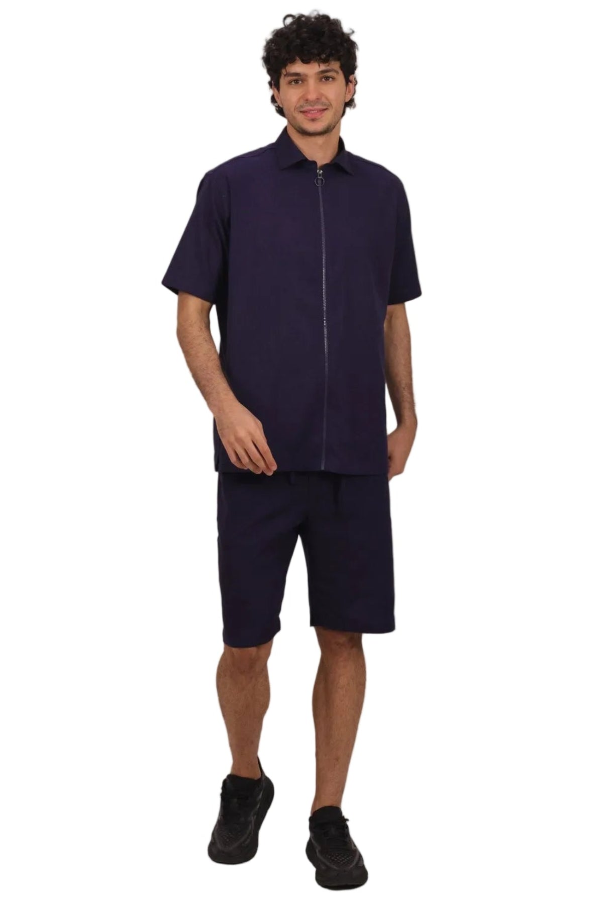 A man modeling a matching dark navy short-sleeve zip-up shirt and shorts set, paired with black sneakers, against a solid white background.