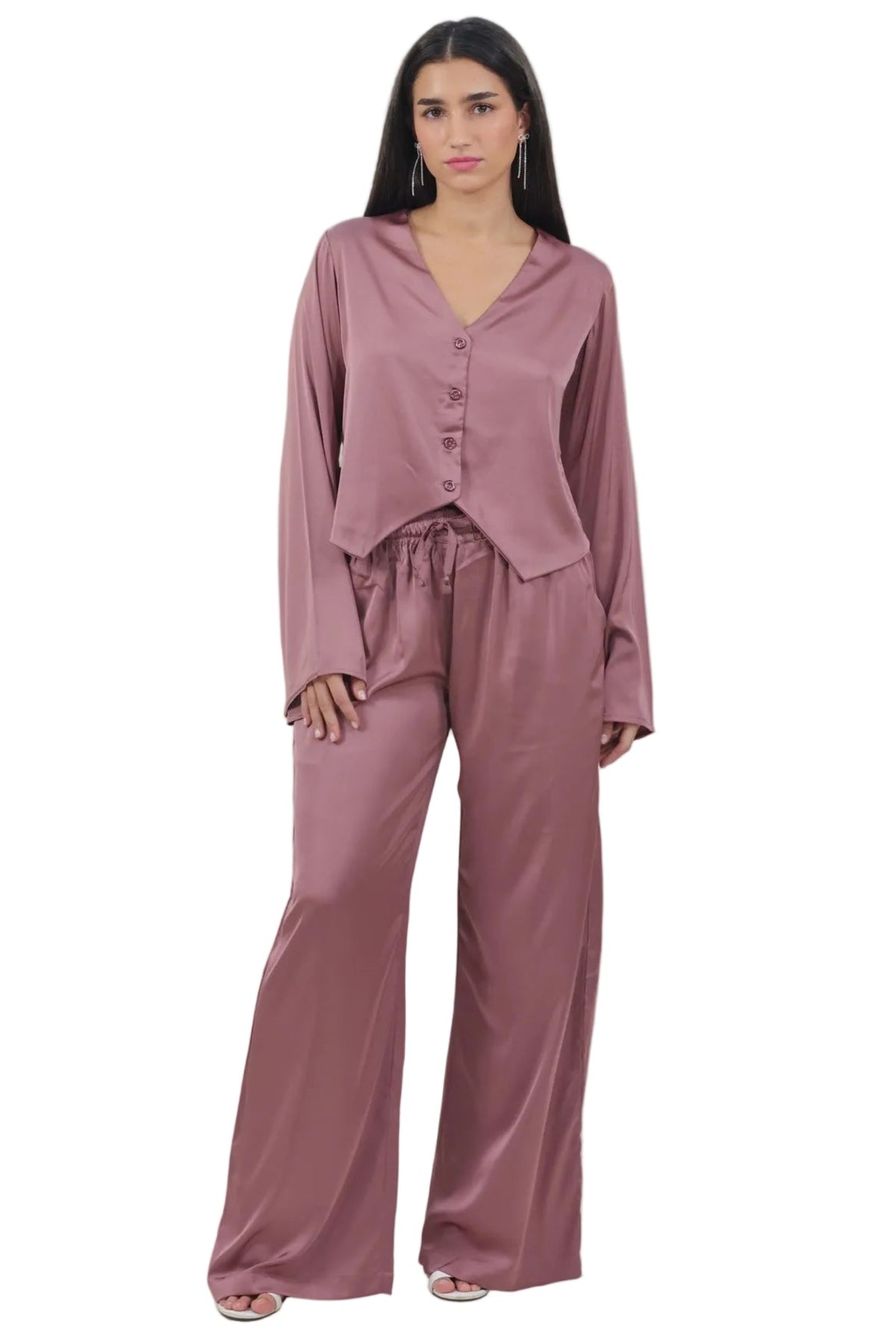 A woman modeling a dusty rose satin pajama set consisting of a long-sleeve button-front top and matching wide-leg pants, shot against a plain white background.