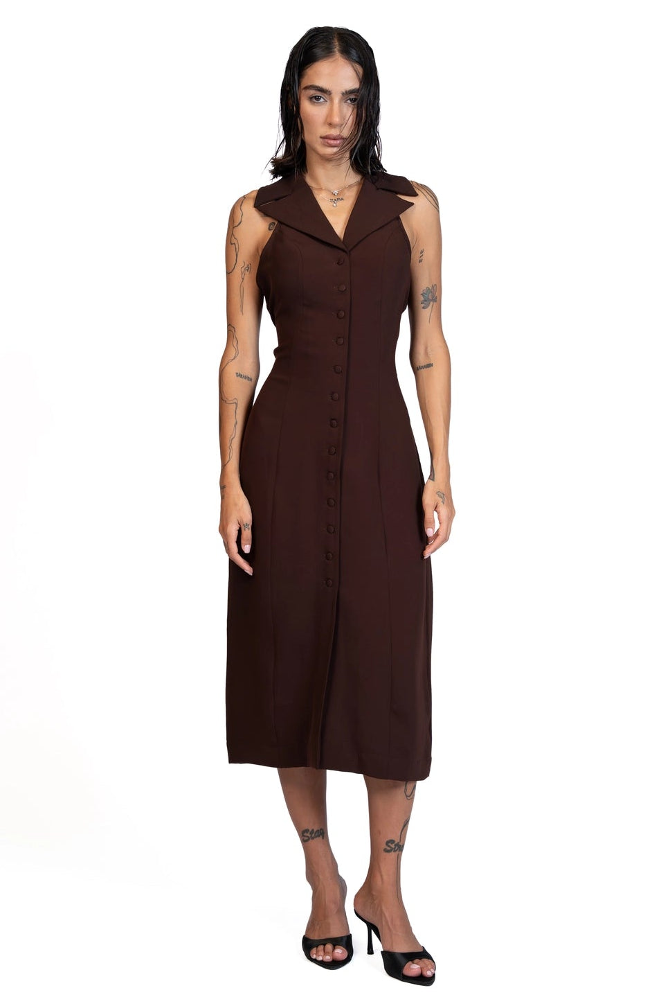 A woman modeling a sleeveless dark brown midi dress with a pointed collar and button-front detail, standing against a plain white background.