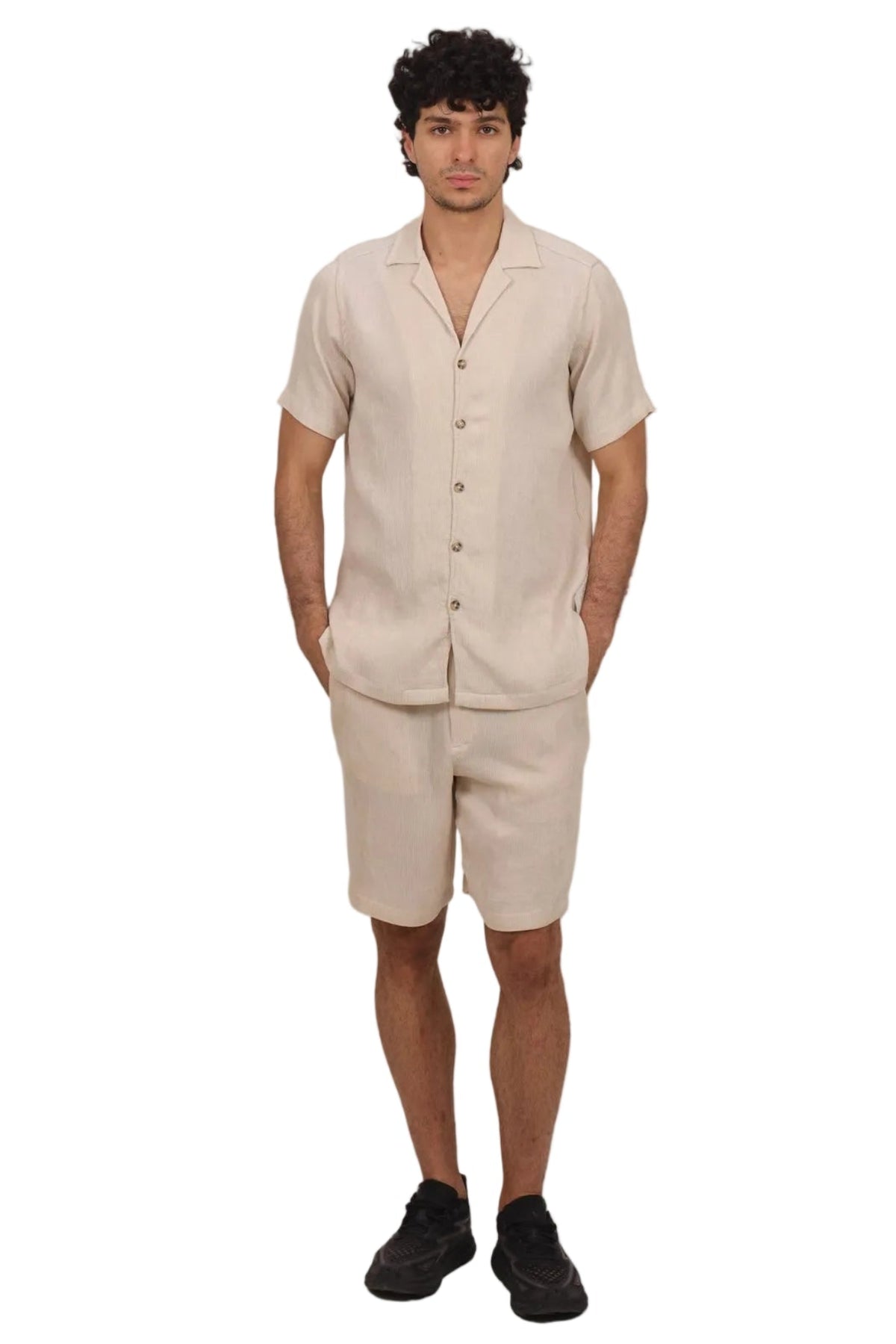 A man modeling a light beige linen short-sleeve button-up shirt and matching linen shorts against a solid white background.