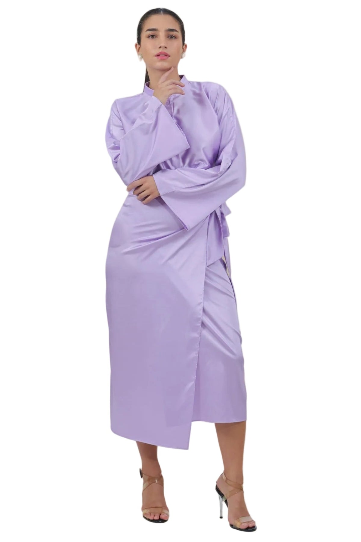 A woman modeling a lavender wrap-style midi dress with long sleeves and a draped waist tie, paired with nude high-heeled sandals, against a plain white background.