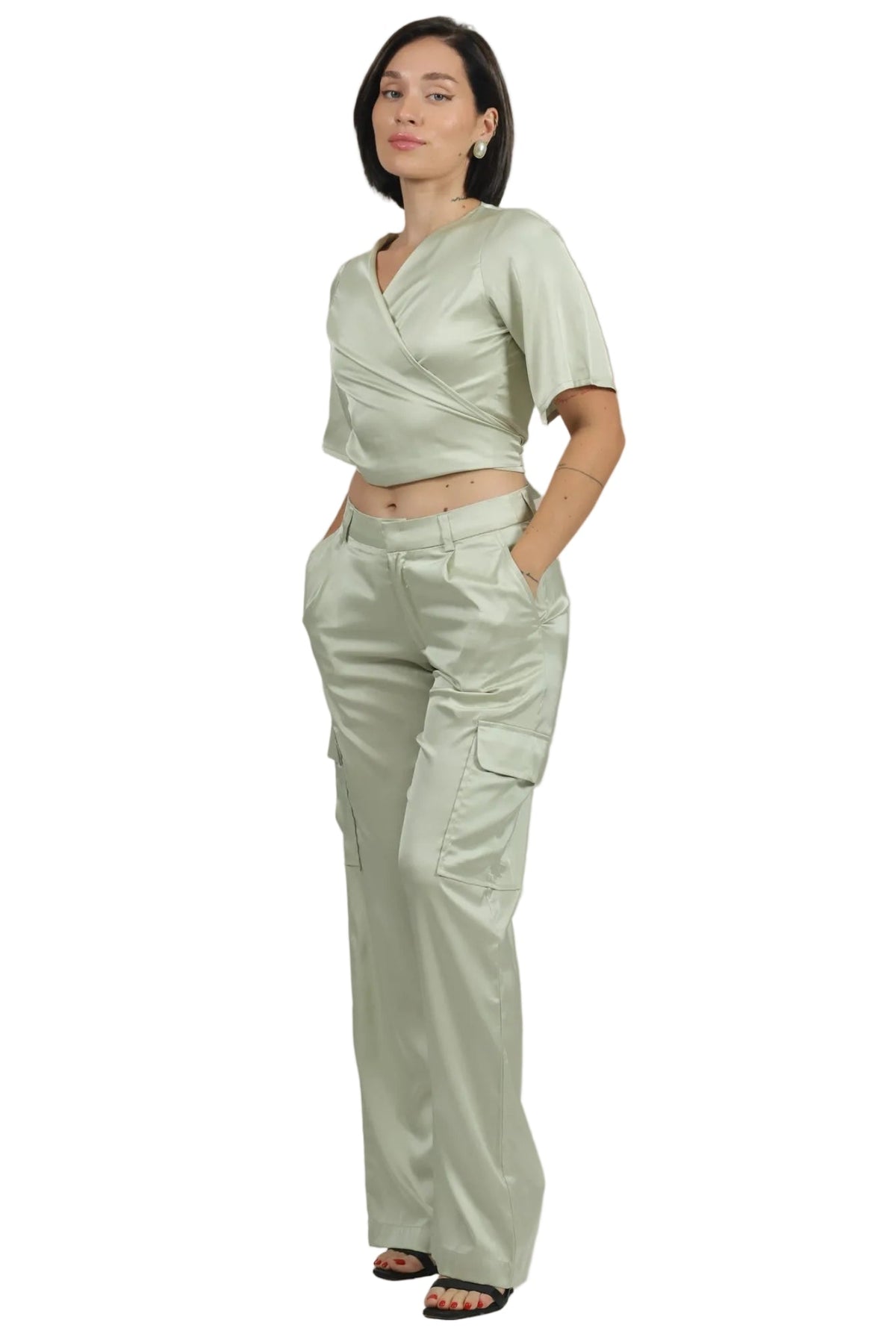 A woman modeling a light sage green two-piece outfit consisting of a short-sleeve wrap-style crop top and matching wide-leg cargo pants, set against a plain white background.