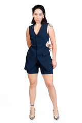 A woman modeling a sleeveless navy blue romper with a wrap-style front and matching shorts, paired with patterned high heels, against a plain white background.