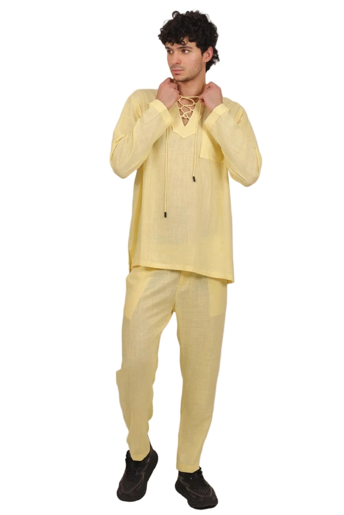 A man modeling a light yellow traditional outfit consisting of a long-sleeve kurta and matching trousers, paired with black shoes, against a solid white background.