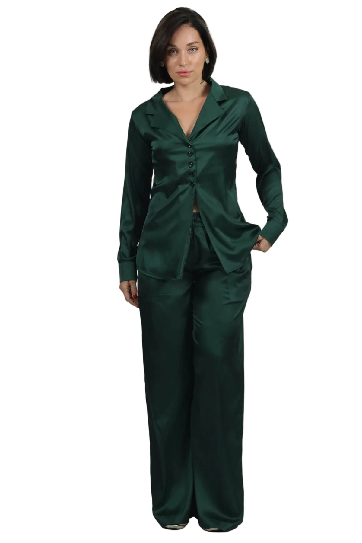 A woman modeling a dark green satin pajama set consisting of a long-sleeve button-front top and matching wide-leg pants, shot against a plain white background.