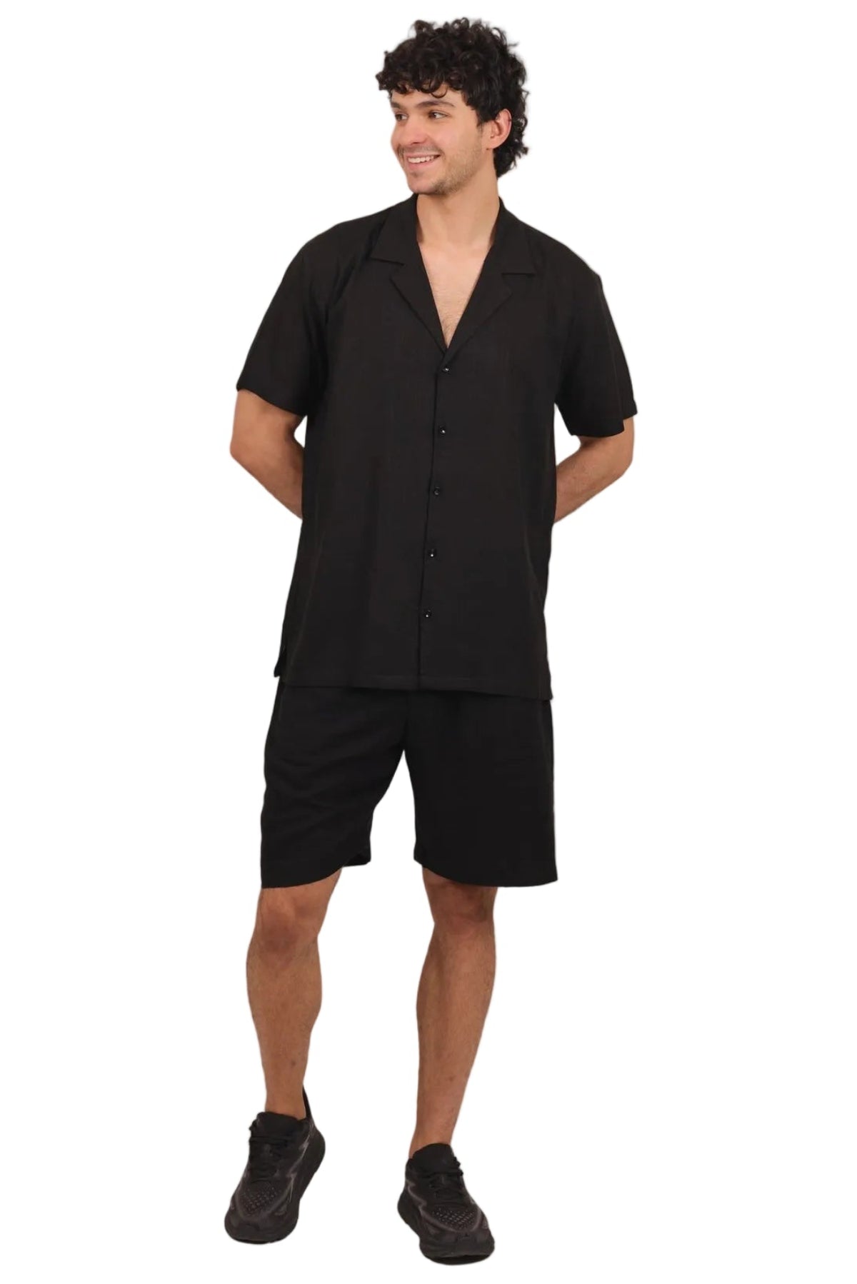 A man modeling a black short-sleeve button-up shirt and matching black shorts against a solid white background.