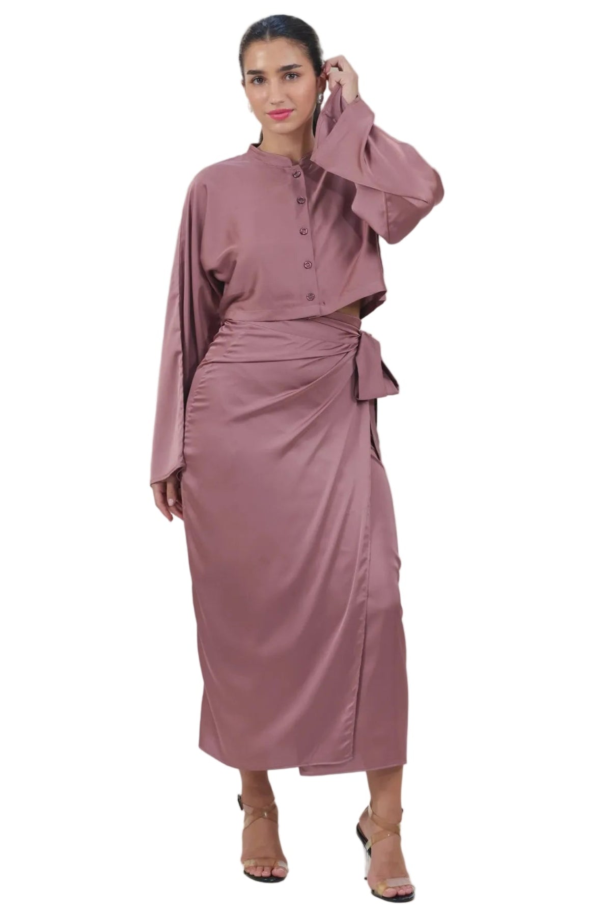 A woman modeling a dusty rose long-sleeved maxi dress with a high collar, buttoned front, and a matching fabric tie belt at the waist, set against a plain white background.