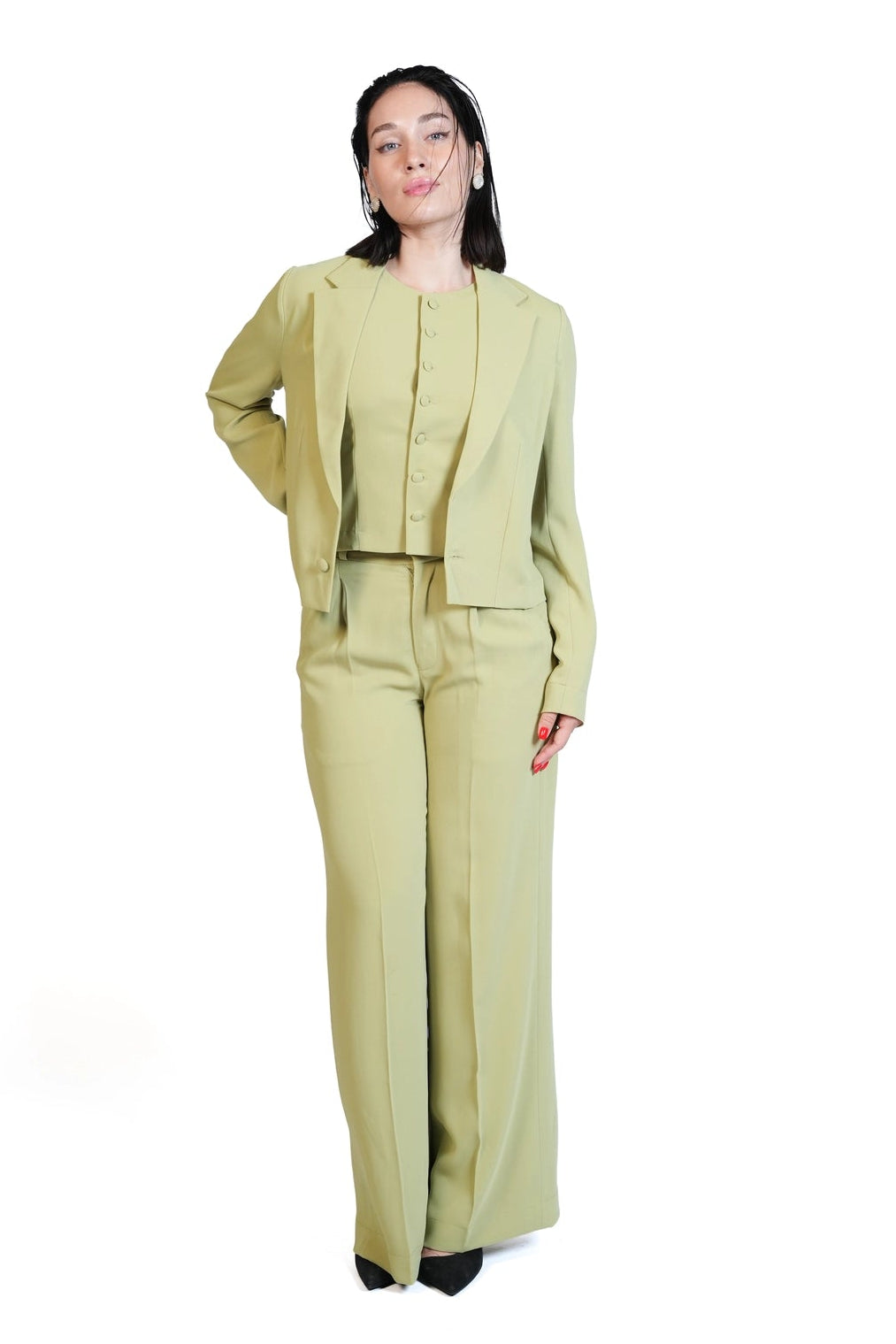 A woman modeling a light olive green two-piece suit consisting of a cropped jacket and matching wide-leg trousers, set against a plain white background.