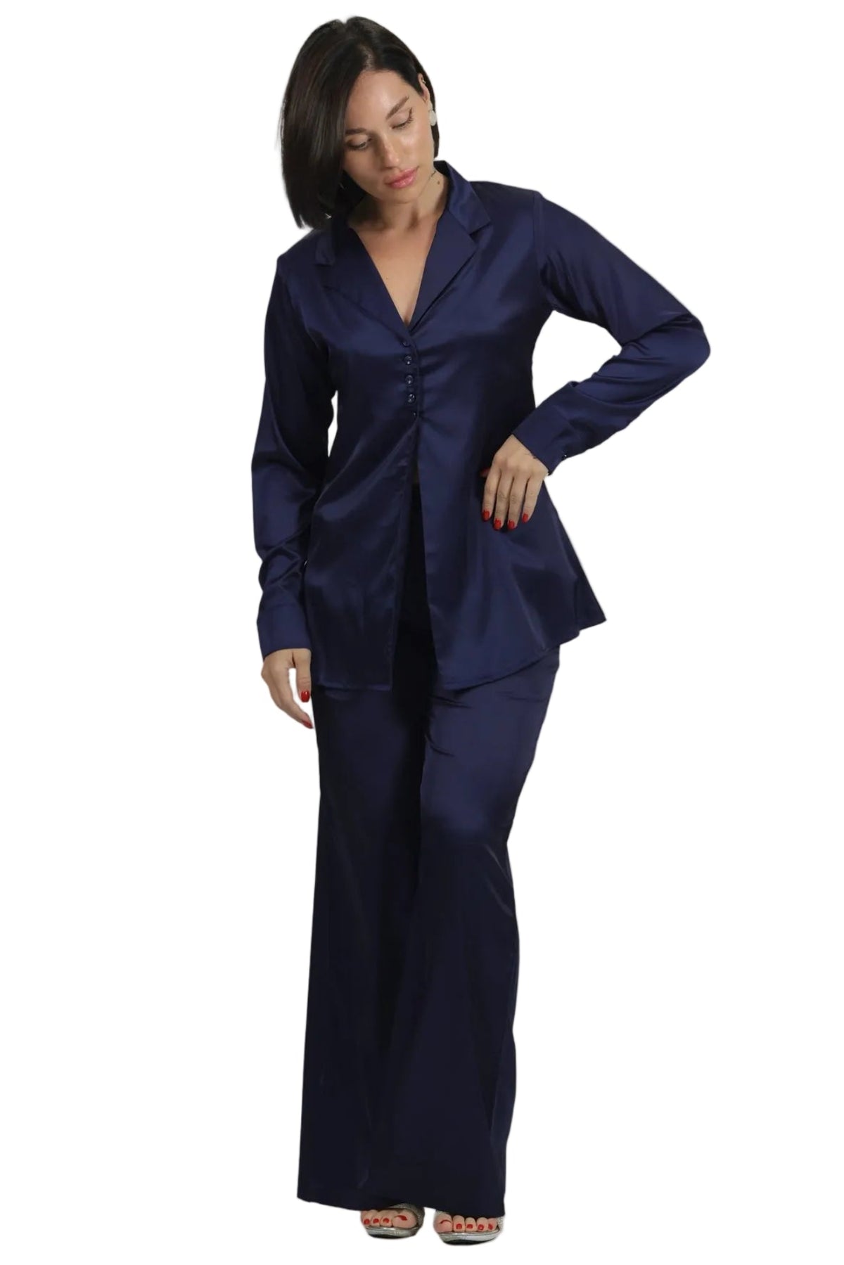 A woman modeling a navy blue satin two-piece pajama set consisting of a long-sleeve button-up top and matching wide-leg pants, set against a plain white background.