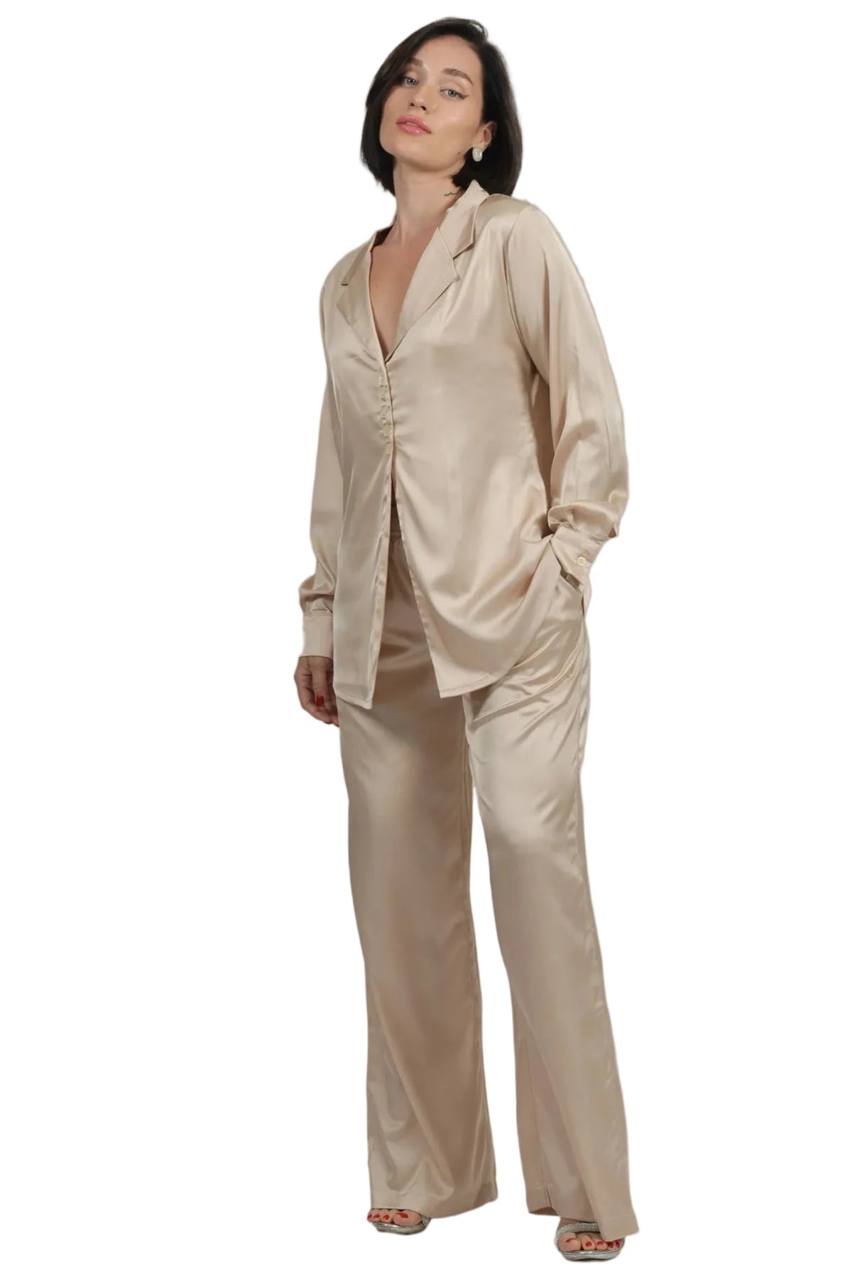 A woman modeling a matching beige satin pajama set with a long-sleeve button-front top and wide-leg pants, photographed against a plain white background.