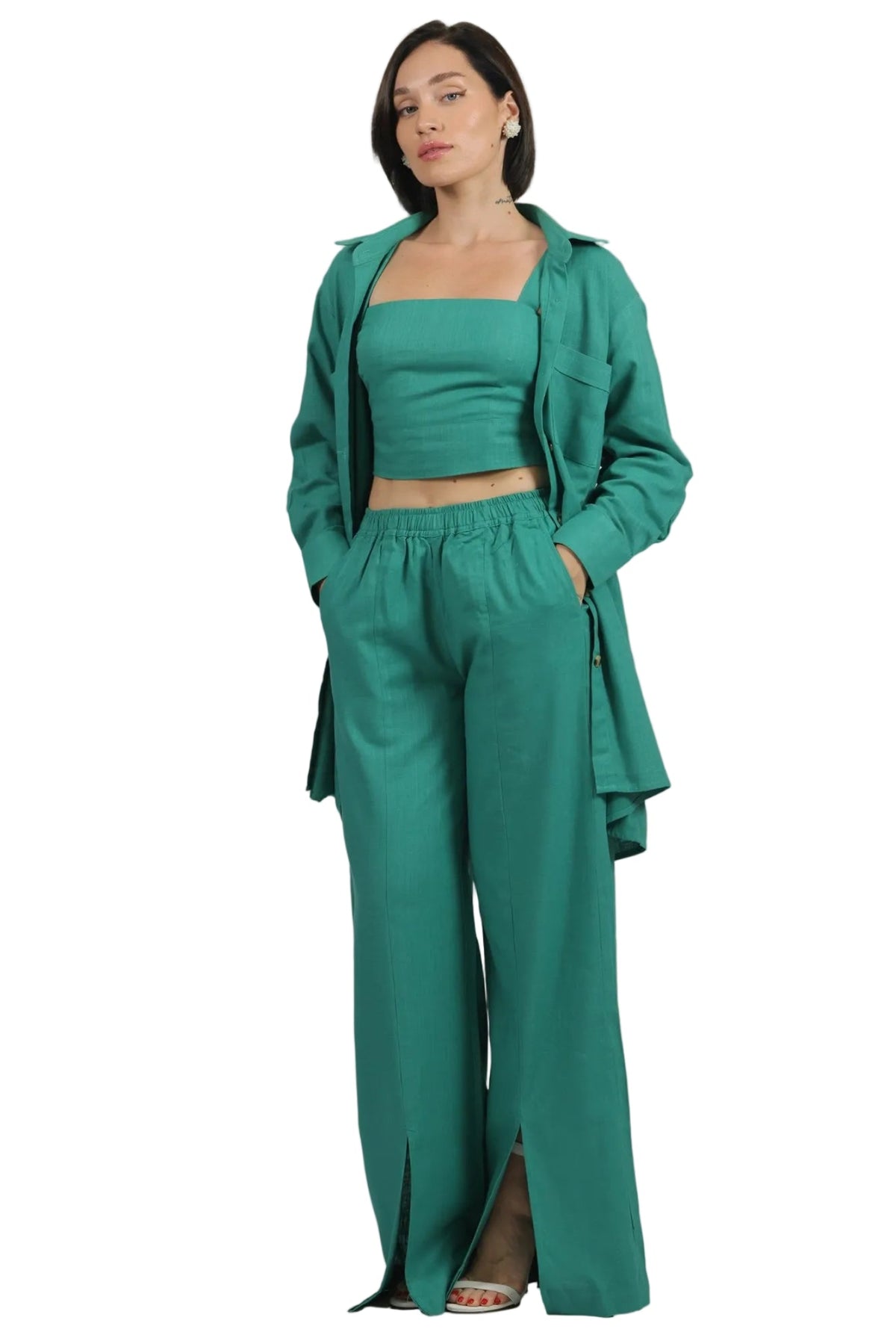 A woman modeling a matching teal green three-piece outfit consisting of a cropped tank top, wide-leg trousers with front slits, and an open longline blazer, set against a plain white background.