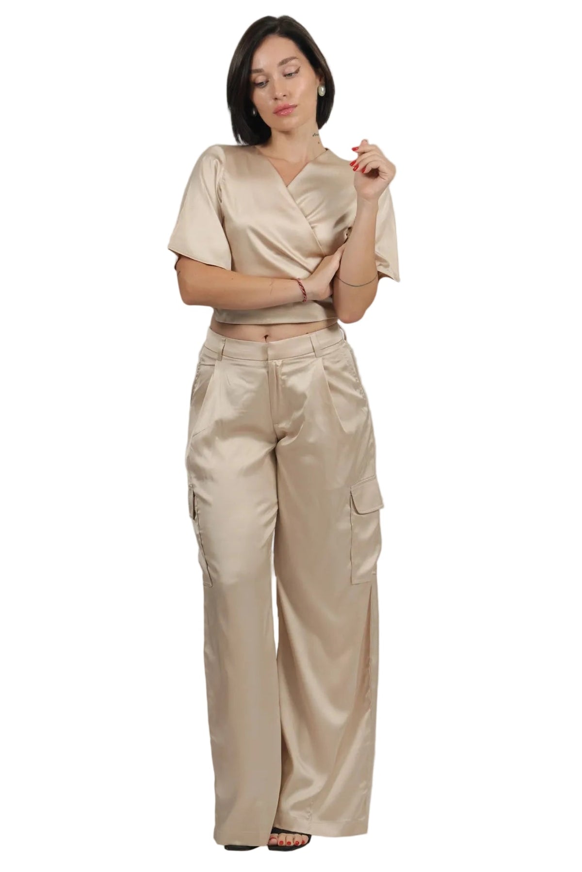 A woman modeling a matching beige satin two-piece set consisting of a short-sleeve wrap-style top and high-waisted wide-leg cargo pants, shot against a solid white background.