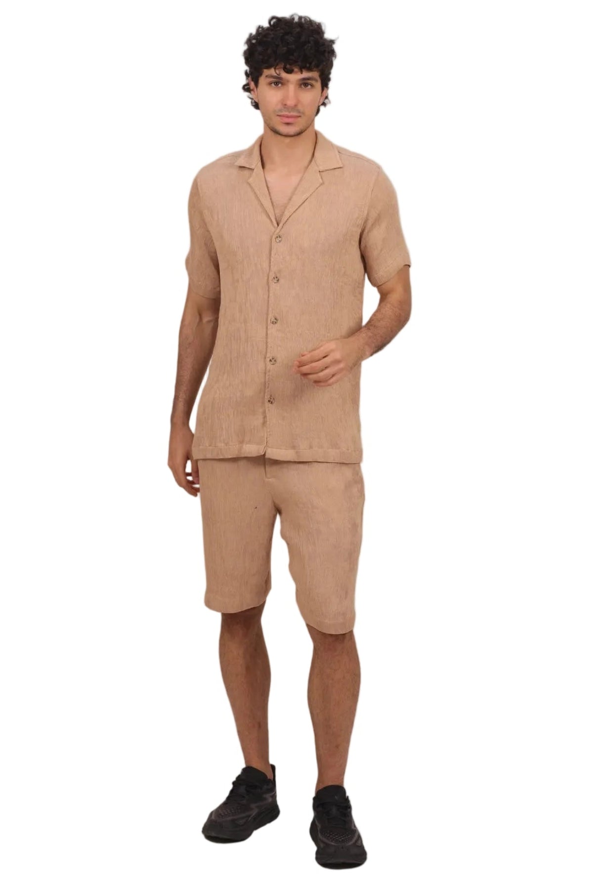 A man modeling a light beige linen short-sleeve button-up shirt and matching linen shorts, paired with black sneakers, against a solid white background.