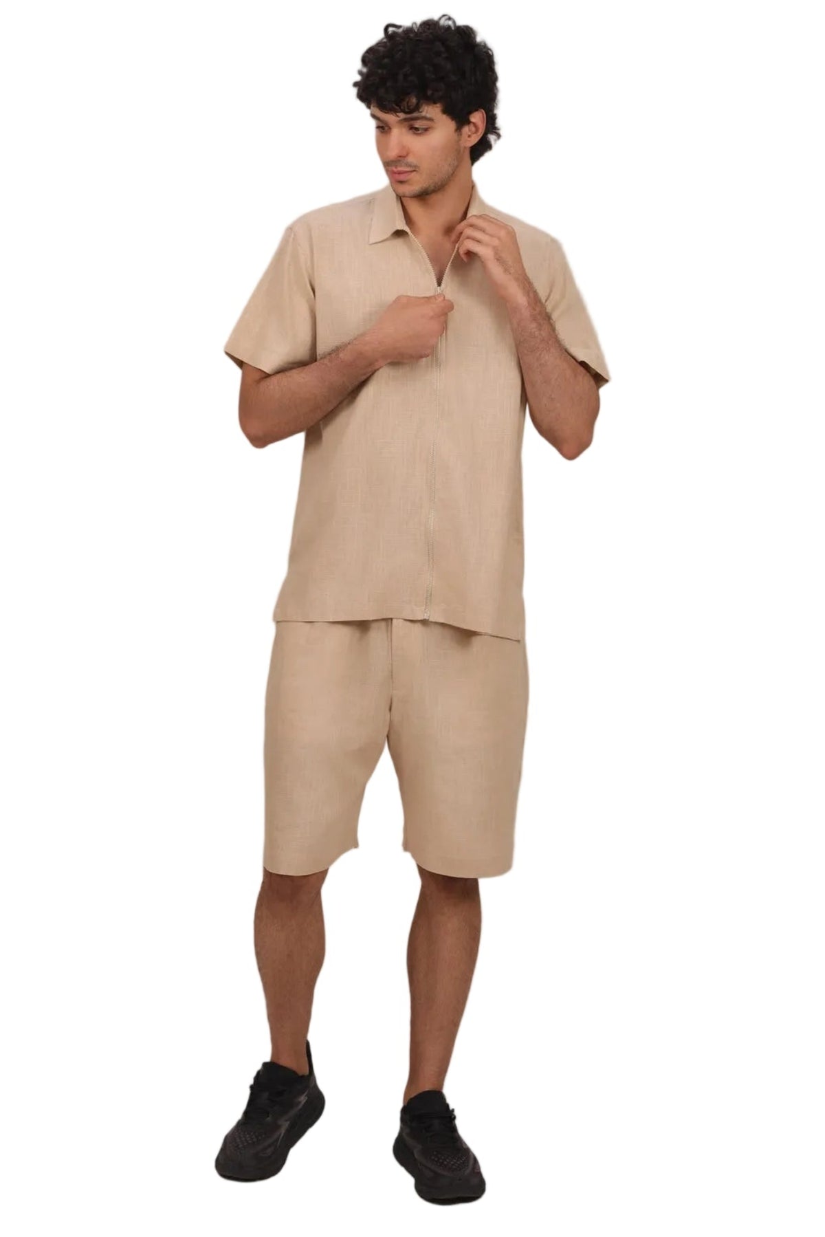 A man modeling a matching beige linen short-sleeve button-up shirt and shorts set, paired with black sneakers, against a solid white background.