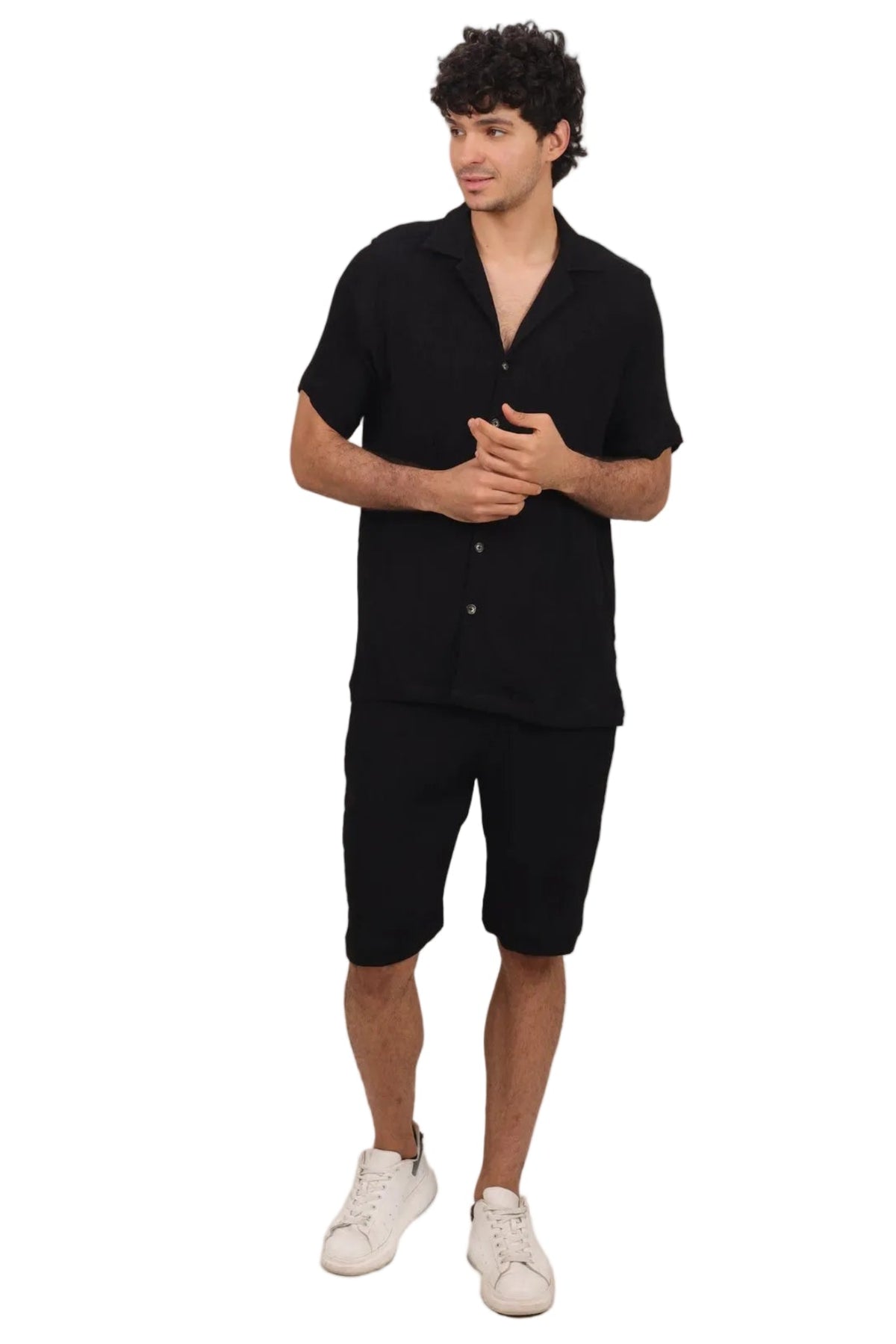 A man modeling a black short-sleeve button-up shirt and matching black shorts, paired with white sneakers, against a solid white background.