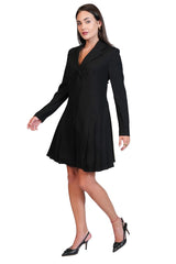A woman modeling a black long-sleeve mini dress with a structured collar and flared skirt, paired with black pointed-toe heels, against a plain white background.
