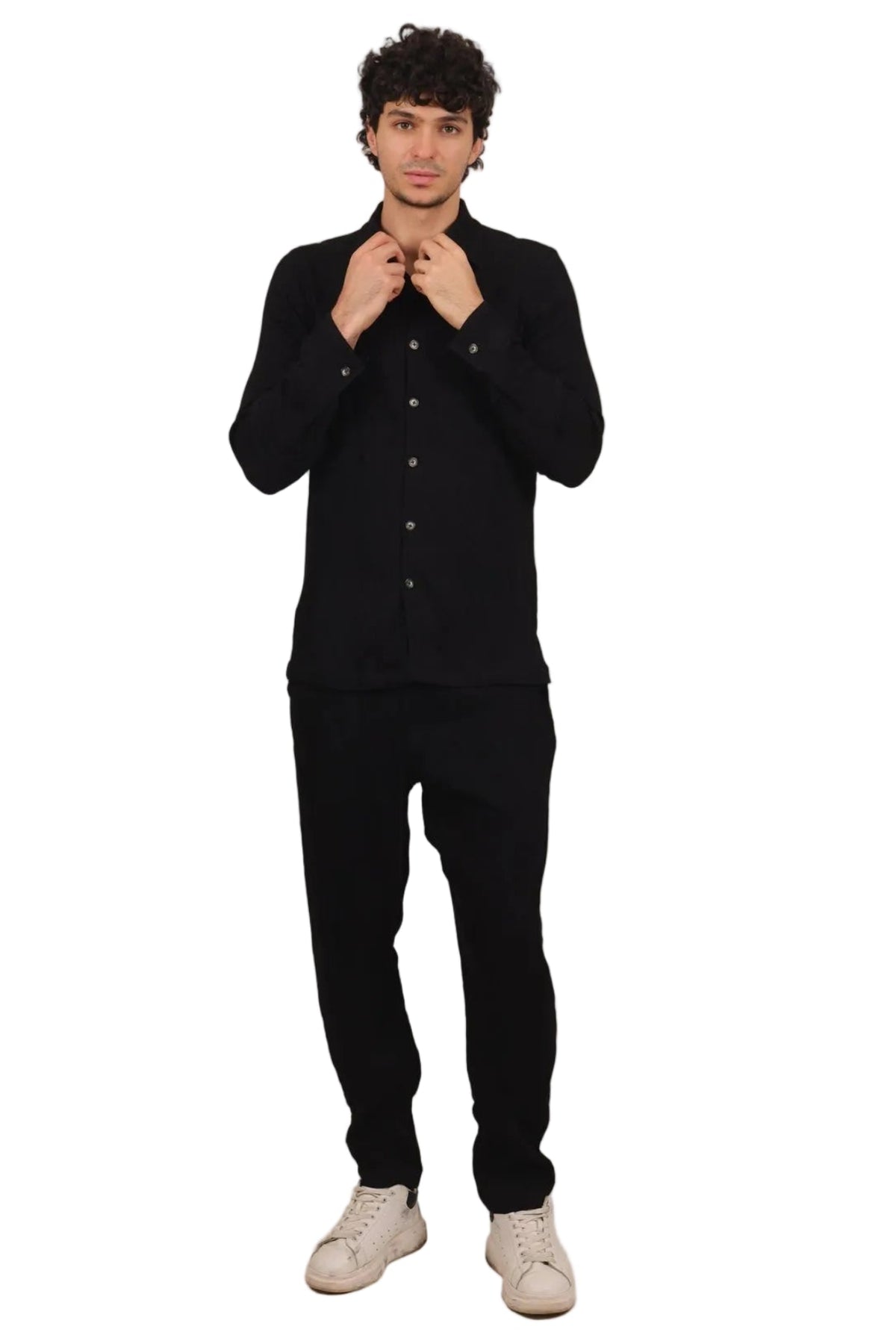 A man wearing a black long-sleeve button-up shirt, black pants, and off-white sneakers, standing against a solid white background.