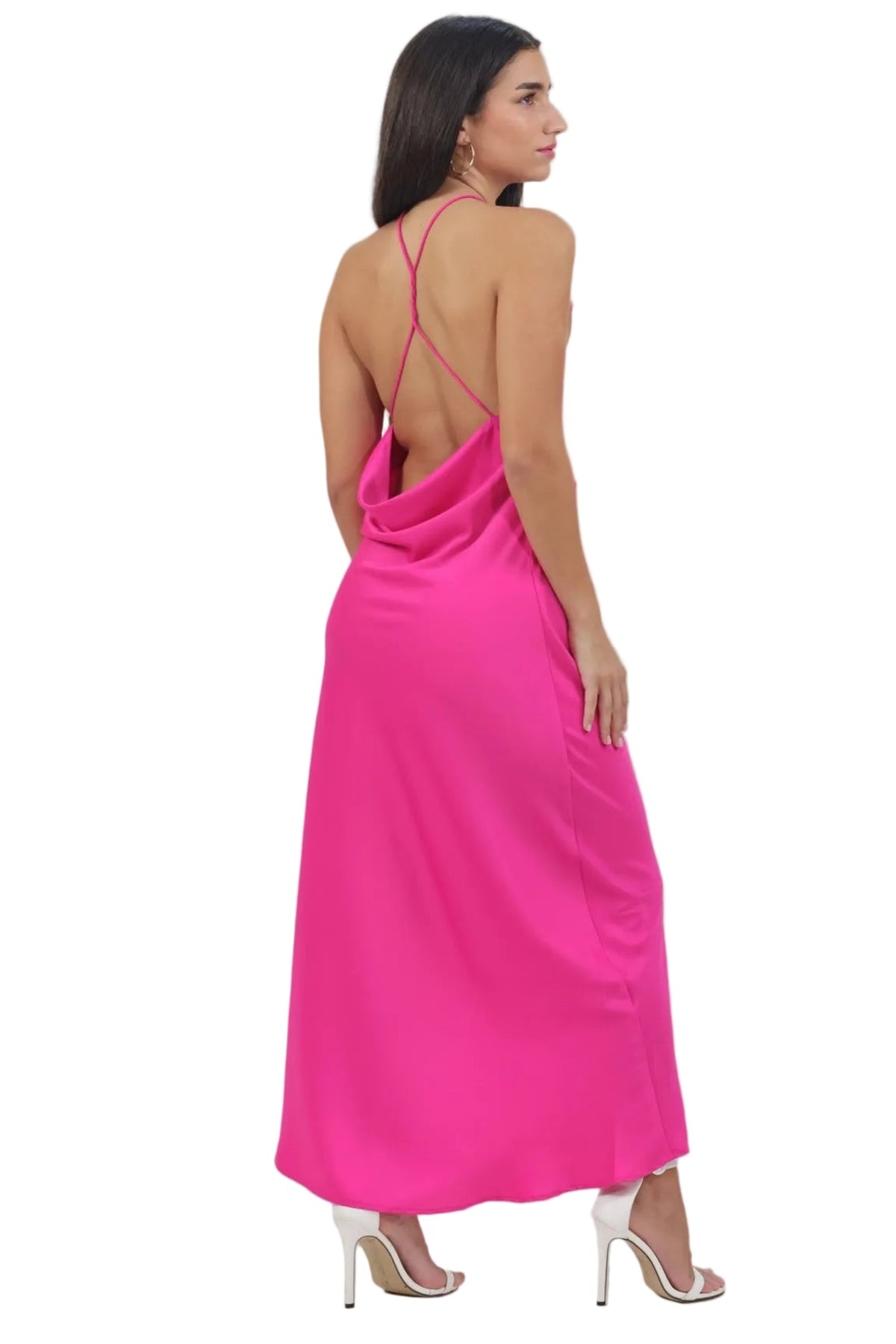 A woman modeling a bright pink satin maxi dress from the back, featuring thin spaghetti straps, a draped open back, and side pockets, set against a plain white background.