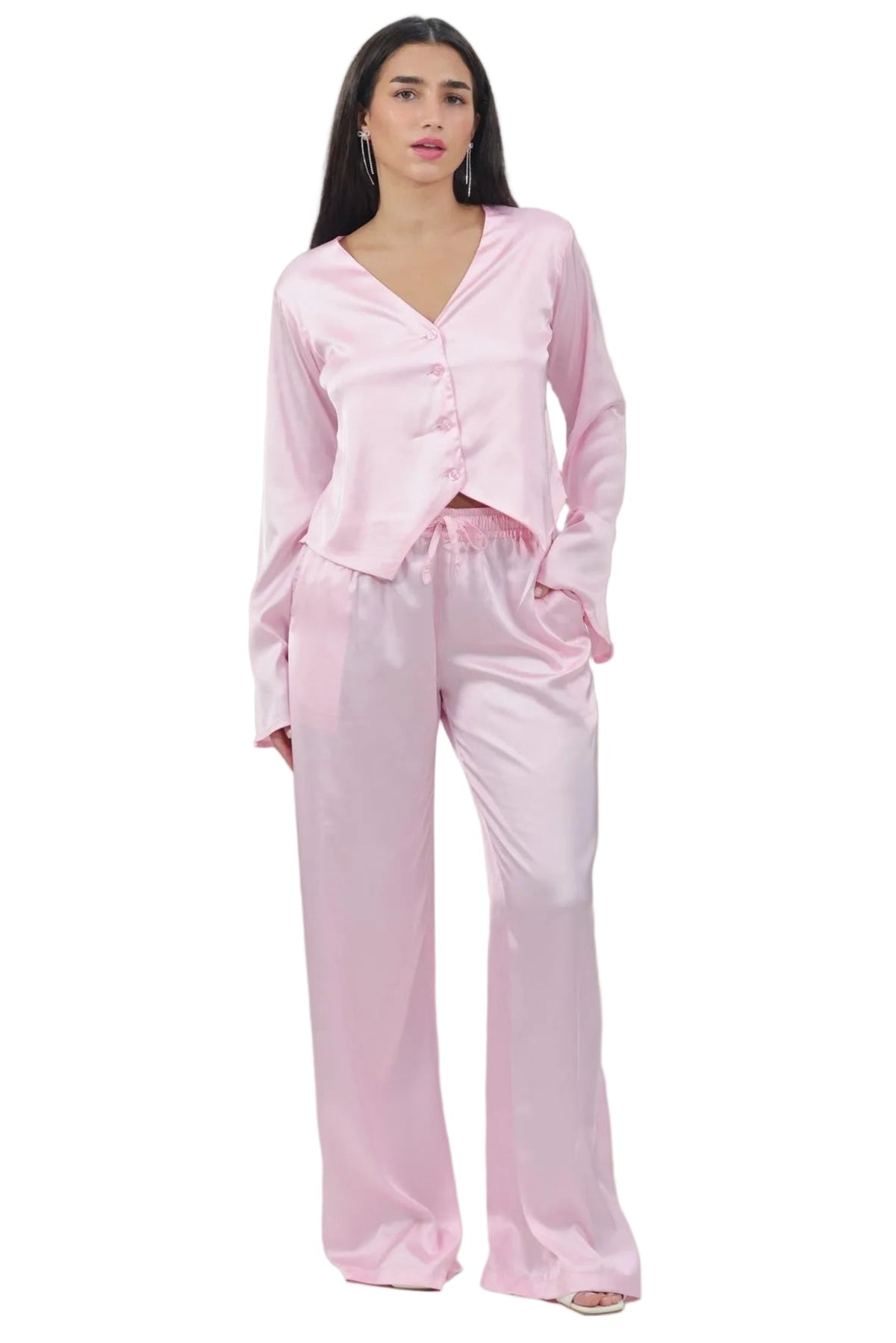 A woman modeling a two-piece satin pajama set in light pink, featuring a long-sleeve button-front top and matching wide-leg pants, against a plain white background.