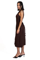 A woman modeling a sleeveless dark brown midi dress with a side tie detail, shown in profile against a solid white background.