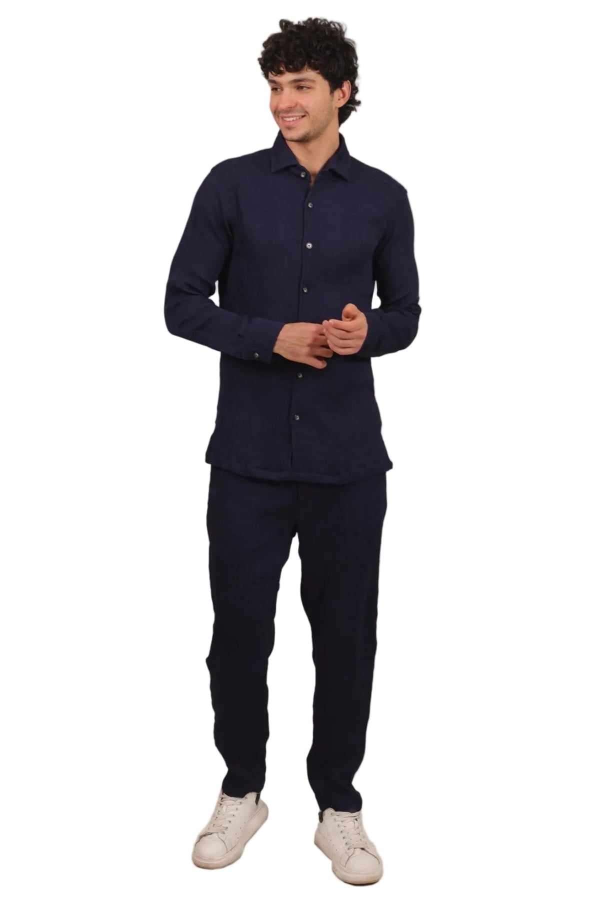 A man modeling a matching dark navy blue two-piece set consisting of a long-sleeve button-up shirt and trousers, paired with off-white sneakers, against a solid white background.