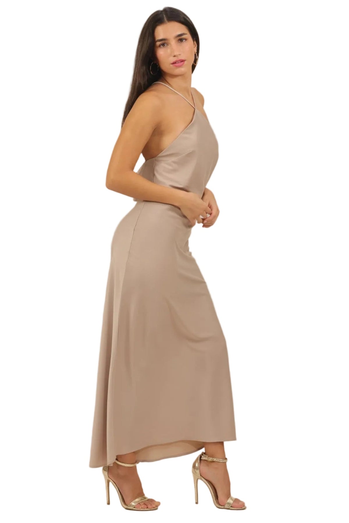 A woman modeling a sleeveless, one-shoulder maxi dress in a light taupe-beige color, paired with matching beige high-heeled sandals, set against a plain white background.