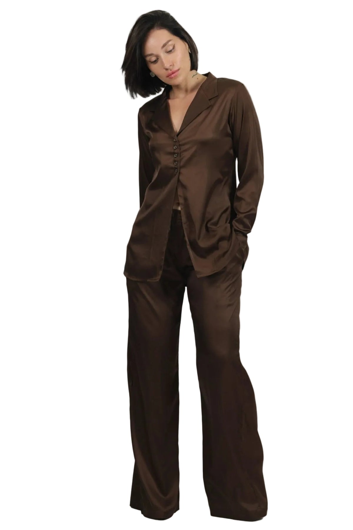A woman modeling a matching dark brown satin pajama set with a long-sleeve button-front top and wide-leg pants against a plain white background.