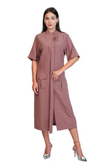 A woman modeling a dusty rose midi dress with short sleeves, a high collar, and front pockets, paired with silver high heels, set against a plain white background.