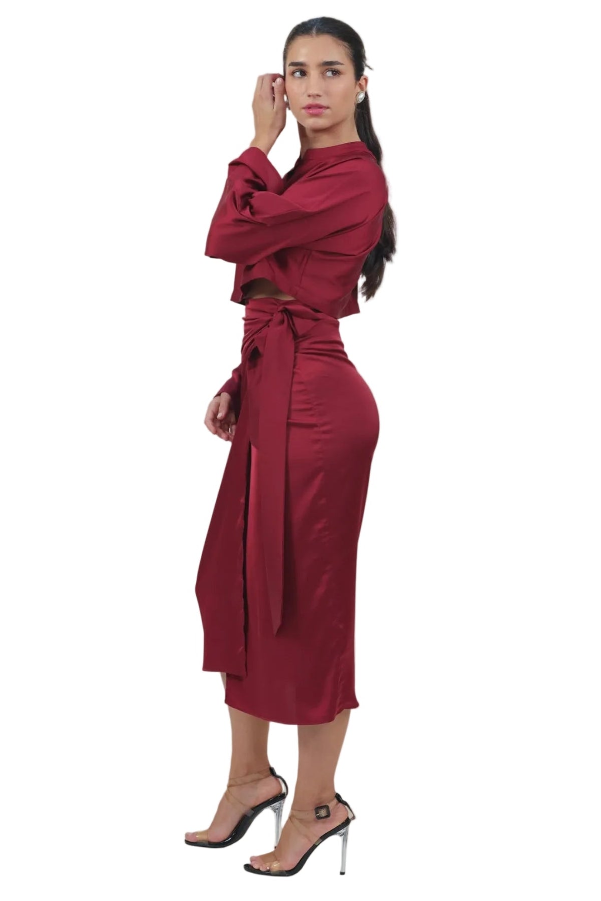 A woman modeling a long-sleeved, high-neck midi dress in a deep burgundy red. The dress features a wrap-style waist with a matching fabric tie belt.